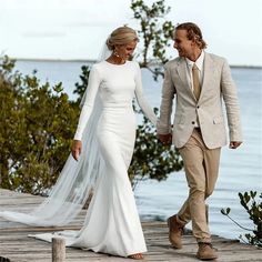 a bride and groom walking on a dock holding each other's hands as they walk towards the water