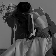 black and white photograph of a man kissing a woman on the cheek with flowers in her lap