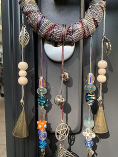 an assortment of beads hanging from a hook on a metal door handle with bells attached to it