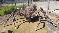 a large spider statue sitting on top of a dirt ground next to a wire fence