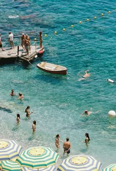 many people are swimming in the ocean with umbrellas