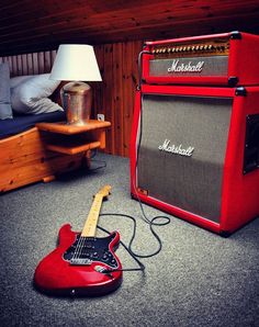 a red guitar and amp sitting on the floor next to a lamp in a room