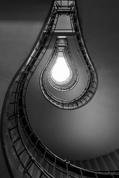 a spiral staircase with a light bulb at the top and bottom in black and white