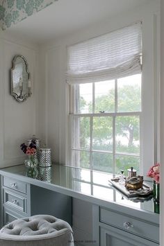 a room with a desk, mirror and stool in it next to a large window