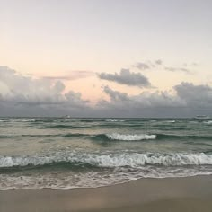 the ocean waves come in to shore as the sun goes down on an overcast day