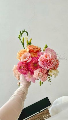 a bride's hand holding a bouquet of pink and orange flowers