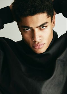 a close up of a person wearing a black shirt and holding his hands on his head