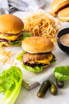 three hamburgers with lettuce, cheese and pickles next to some dipping sauce