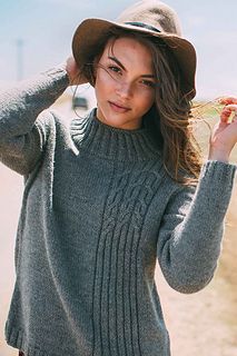 a woman wearing a gray sweater and hat is posing for the camera with her hand on her head