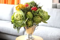 a silver vase filled with lots of green flowers on top of a table next to a couch