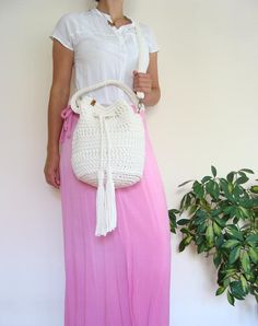 a woman wearing a pink skirt and holding a white handbag next to a potted plant