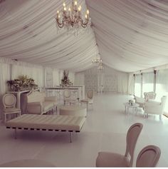 a large room with chairs, tables and chandeliers on the ceiling is decorated in white draping