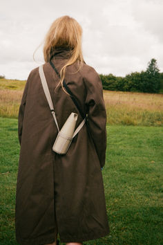 a woman in a brown coat is standing on the grass with her back to the camera