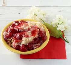 a yellow bowl filled with food on top of a red napkin next to white flowers