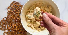 a hand holding a pretzel in front of a bowl of food