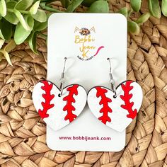 two heart shaped earrings with red and white stitching on them sitting next to a plant