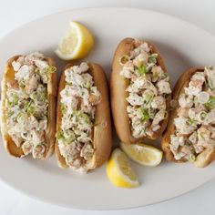 three hot dogs on buns topped with cole slaw and lemon wedges sitting on a white plate