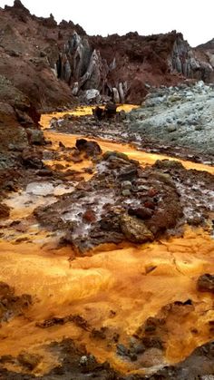 an orange substance is on the ground next to some rocks and water with mountains in the background