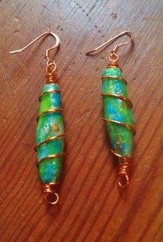 two green and gold earrings sitting on top of a wooden table