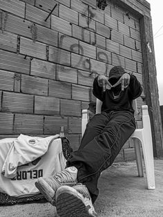 a black and white photo of a person sitting on a chair next to a brick wall