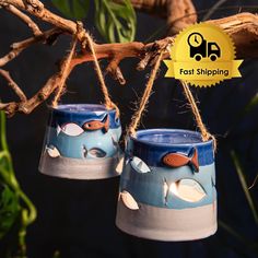 two blue and white vases hanging from a tree branch with fish painted on them