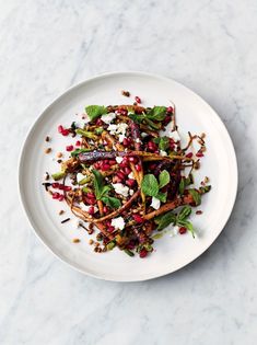 a white plate topped with lots of food on top of a marble countertop next to a knife and fork