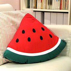 a watermelon pillow sitting on top of a white couch next to a book shelf