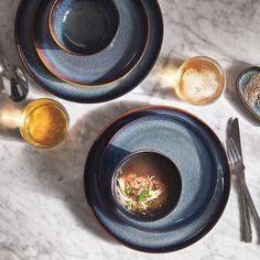 two plates with soup and spoons on a marble table top next to silverware