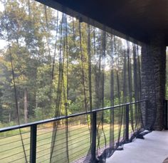 the screened porch is covered with sheer curtains and looks out onto the wooded area in the distance