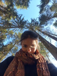 a woman is standing in front of trees wearing a scarf and looking up at the sky