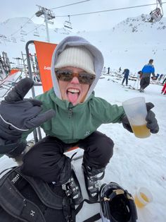 a person sitting on top of a snow covered ski slope holding a beer in their hand