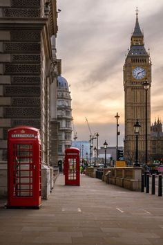 two red telephone booths sitting next to each other on a sidewalk near a clock tower