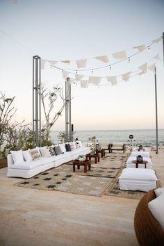 an outdoor seating area with white couches and pillows on the floor next to the ocean