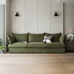 a living room with a large green couch and two lamps on the wall above it