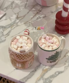 two mugs filled with marshmallows sitting on a table next to candy canes