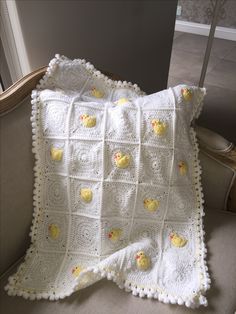 a white crocheted blanket with yellow rubber ducks on it sitting on a chair