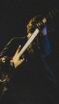 a man playing an electric guitar in the dark with his hand on it's neck