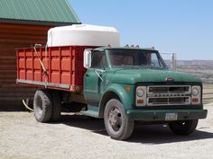 a green and red truck parked in front of a wooden building with a metal roof