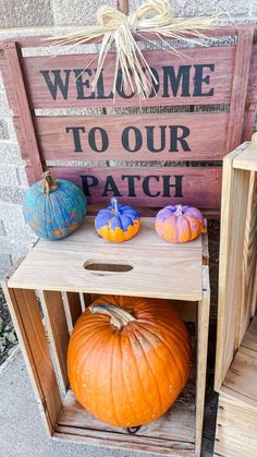 pumpkins and gourds are sitting in wooden crates on the ground near a welcome to our patch sign