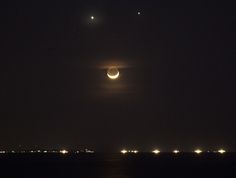 the moon and venus are seen in the night sky over the ocean with lights on