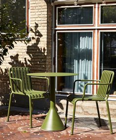 two green chairs and a table in front of a brick building with a large window