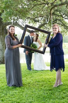 a bride and groom holding up a framed photo in front of their wedding party at the park