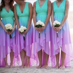 four bridesmaids in blue and purple dresses standing together on the beach with their bouquets