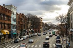 a city street filled with lots of traffic next to tall brown brick buildings and trees