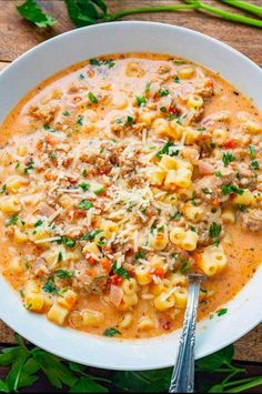 a white bowl filled with pasta and meat soup on top of a wooden table next to green onions