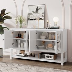 a white cabinet with plates and bowls on it next to a potted plant in the corner