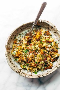 a bowl filled with food sitting on top of a white marble counter next to a spoon