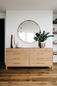 a wooden dresser with a round mirror on it's wall above it and a potted plant in front of it