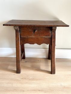 an old wooden table sitting on top of a hard wood floor next to a wall