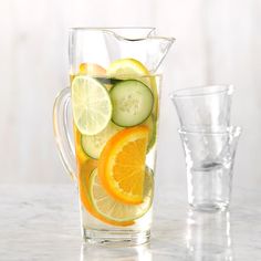 a pitcher filled with cucumbers, oranges and lemon slices next to two glasses